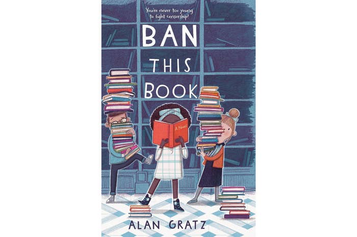 Cover of the book &quot;Ban This Book&quot; by Alan Gratz shows three children carrying stacks of books with one child reading a large red book in the center