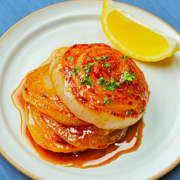 焼き目がついたスライスされた玉ねぎの重ね焼きが皿に乗り、レモンのくし切りが添えられています。