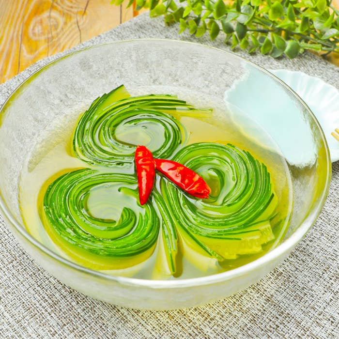 ガラスのボウルに、緑色の野菜や唐辛子がエレガントに盛り付けられている料理。