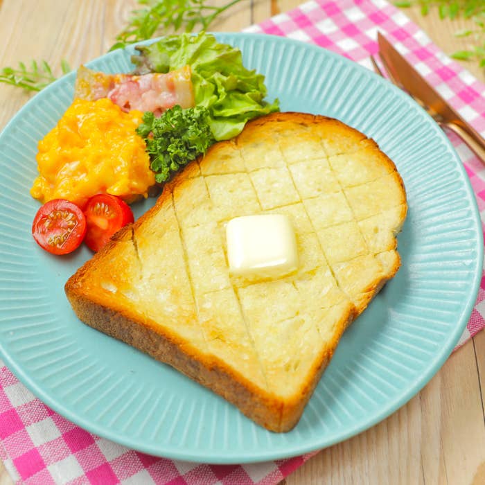 パンにバター、サラダ、スクランブルエッグ、トマトが添えられた朝食プレート。