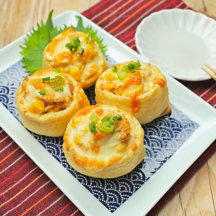 白い皿に盛られた3つの油揚げ料理があり、上にはネギとチーズがトッピングされています。隣には小皿があります。