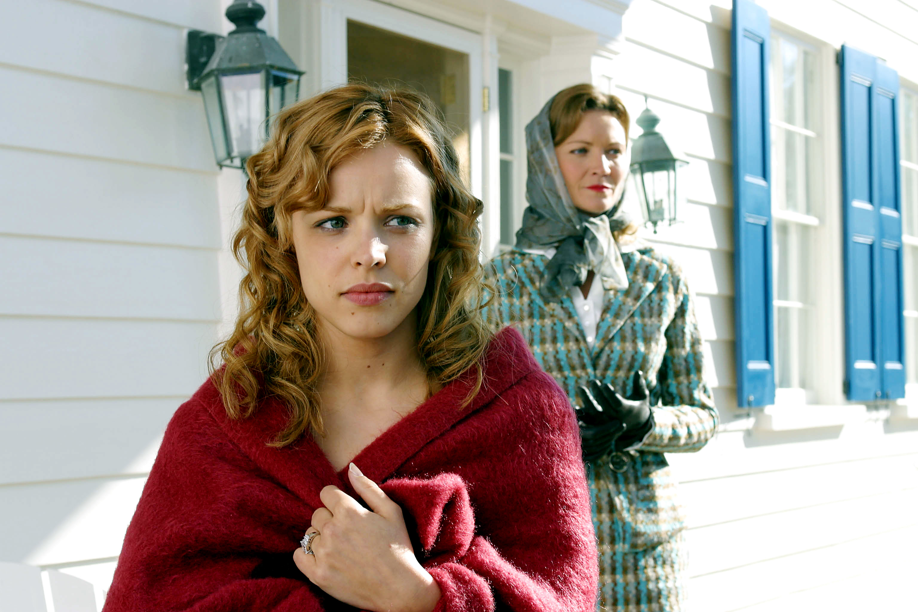 Rachel McAdams, in a red wrap, stands in front of a house with Gena Rowlands in a plaid coat and headscarf behind her. The scene suggests an emotional moment