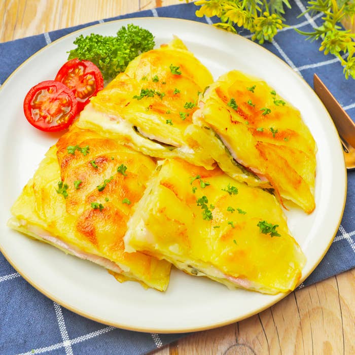 おいしそうなポテトが4つの切れ端に分けられ、トマトのスライスとパセリが添えられたお皿が木製のテーブルに置かれています。