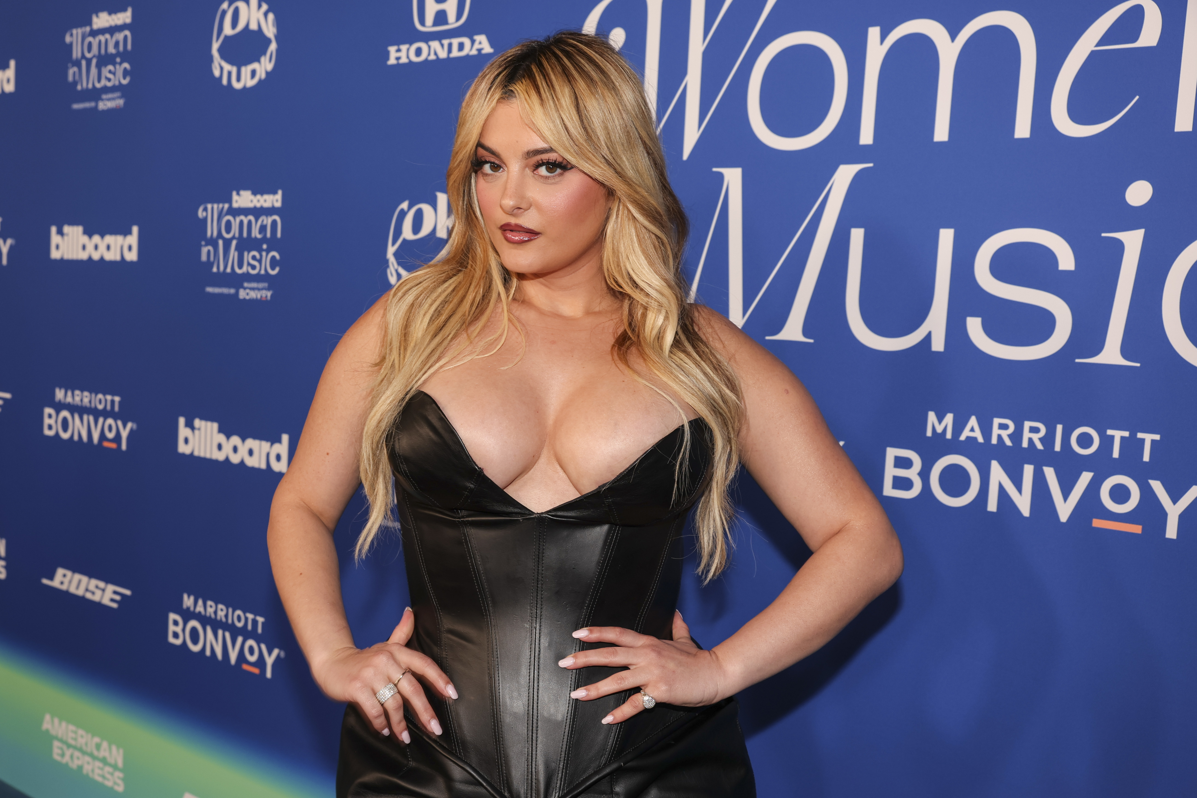 Bebe Rexha at a Billboard Women in Music event, wearing a strapless black leather dress with a sweetheart neckline, posing on the red carpet