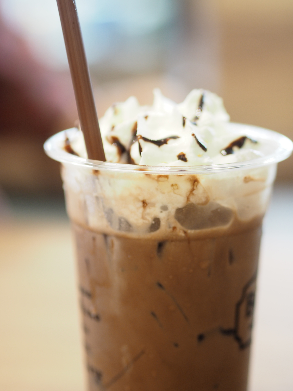 Iced coffee topped with whipped cream and chocolate drizzle in a clear plastic cup with a straw