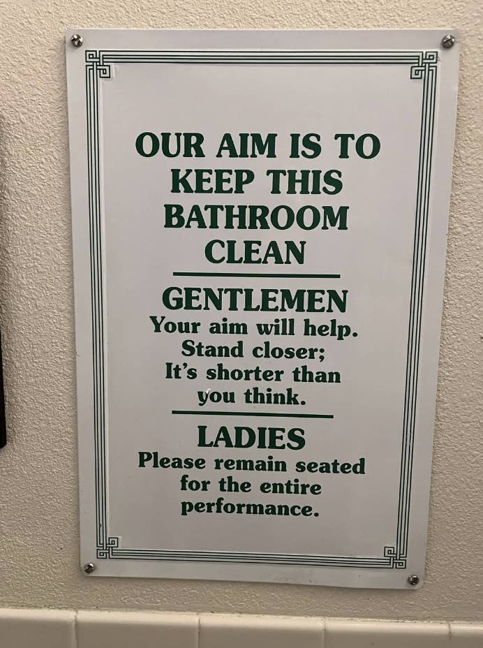 Sign reads: "Our aim is to keep this bathroom clean. Gentlemen, your aim will help. Stand closer; it’s shorter than you think. Ladies, please remain seated for the entire performance."