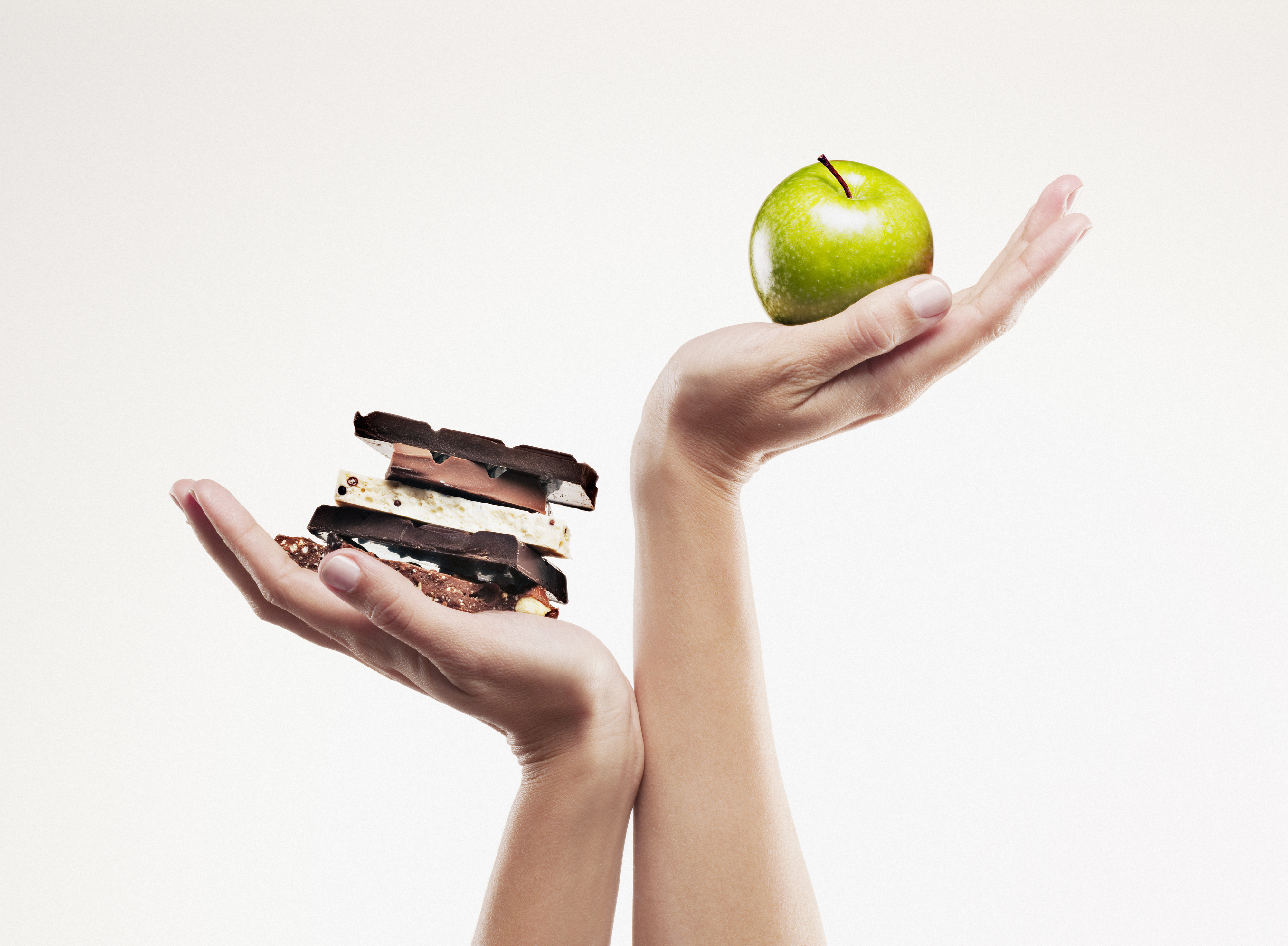 Two hands: one holding an apple and the other holding stacked chocolate bars