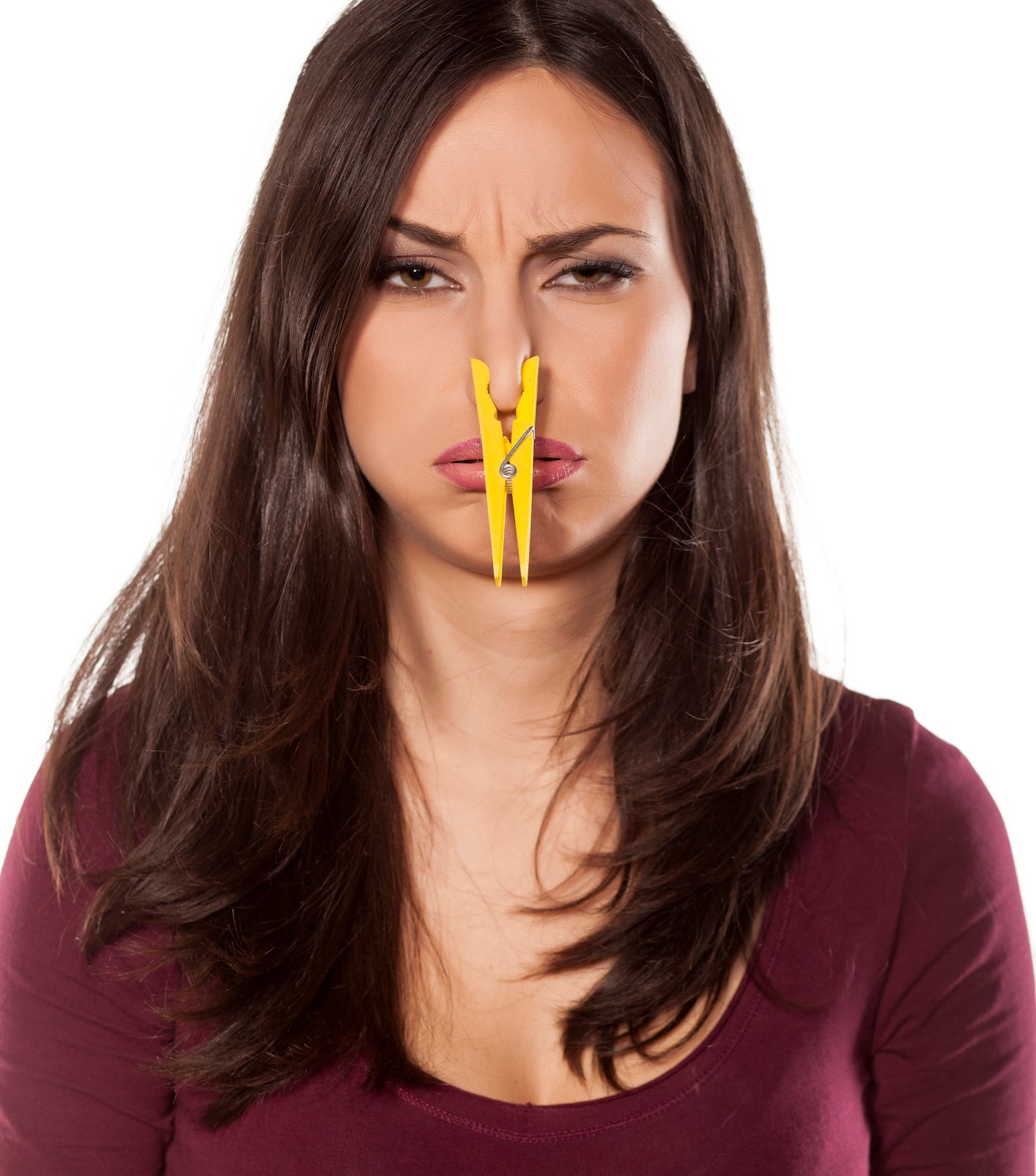 A woman with long hair has a clothespin clipped on her nose with a displeased expression