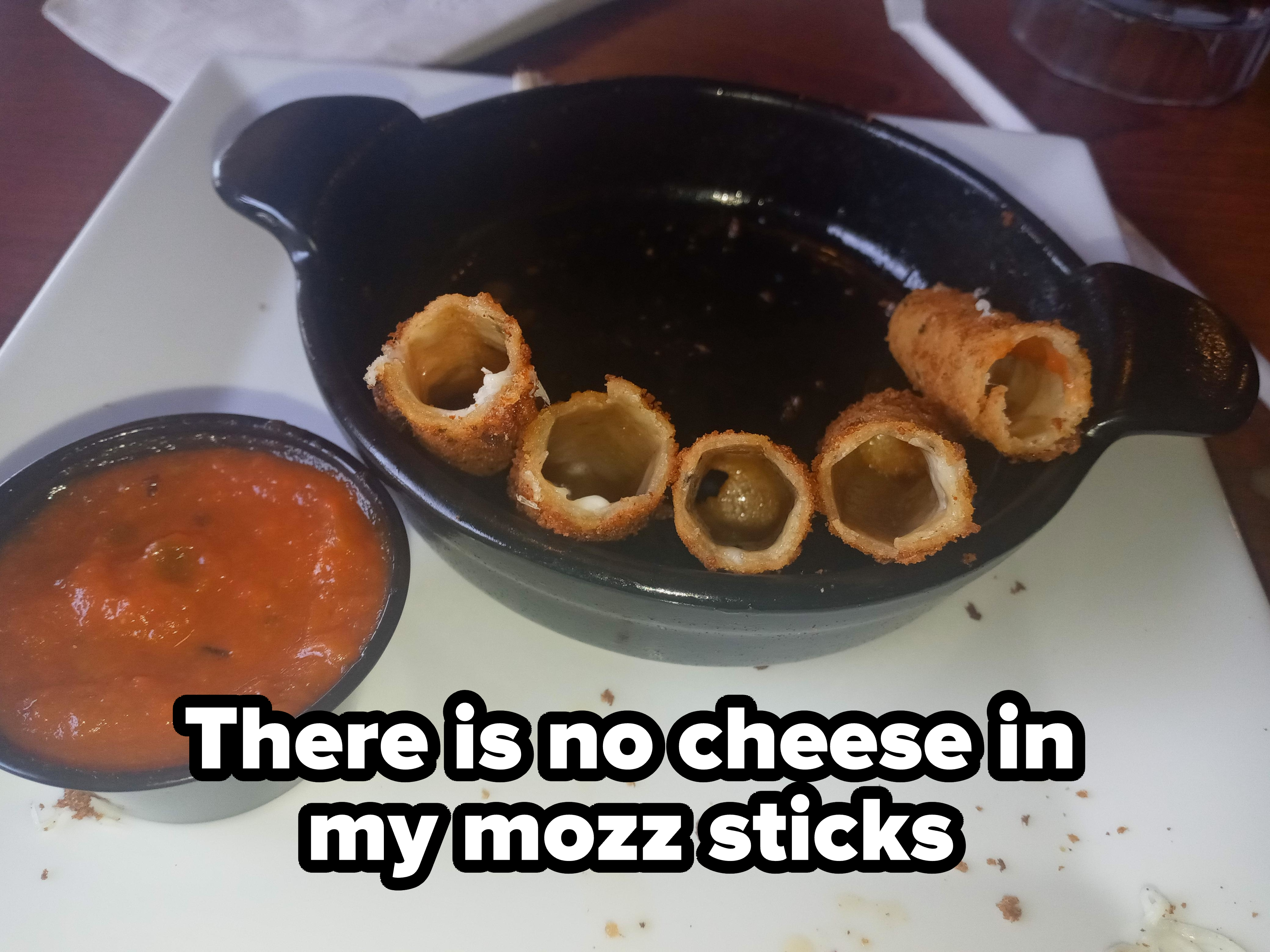 An empty dish with five hollow, breaded rolls and a small container of marinara sauce on the side, placed on a table