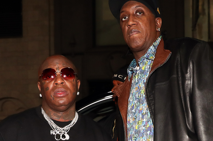 Birdman in a necklace with multiple diamond chains stands next to Slim dressed in a leather jacket and patterned shirt at a music event
