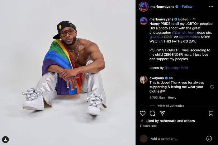Marlon Wayans poses seated, draped in a rainbow flag, wearing sunglasses, a black cap, and silver pants. Instagram post celebrates LGBTQ+ Pride. Comments visible