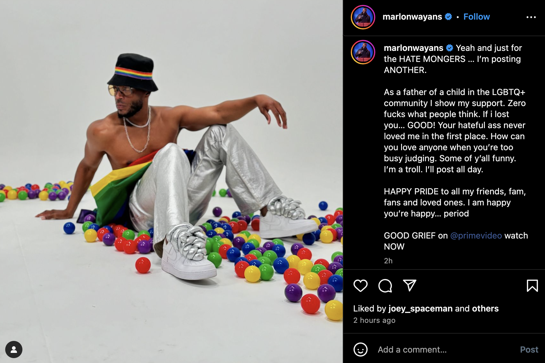 Marlon Wayans sits shirtless on the floor among colorful plastic balls, wearing white pants, silver shoes, and a multicolored hat. Instagram post caption mentions supporting the LGBTQ+ community
