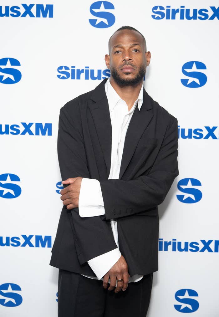 Marlon Wayans poses in a casual suit jacket and white shirt in front of a SiriusXM backdrop