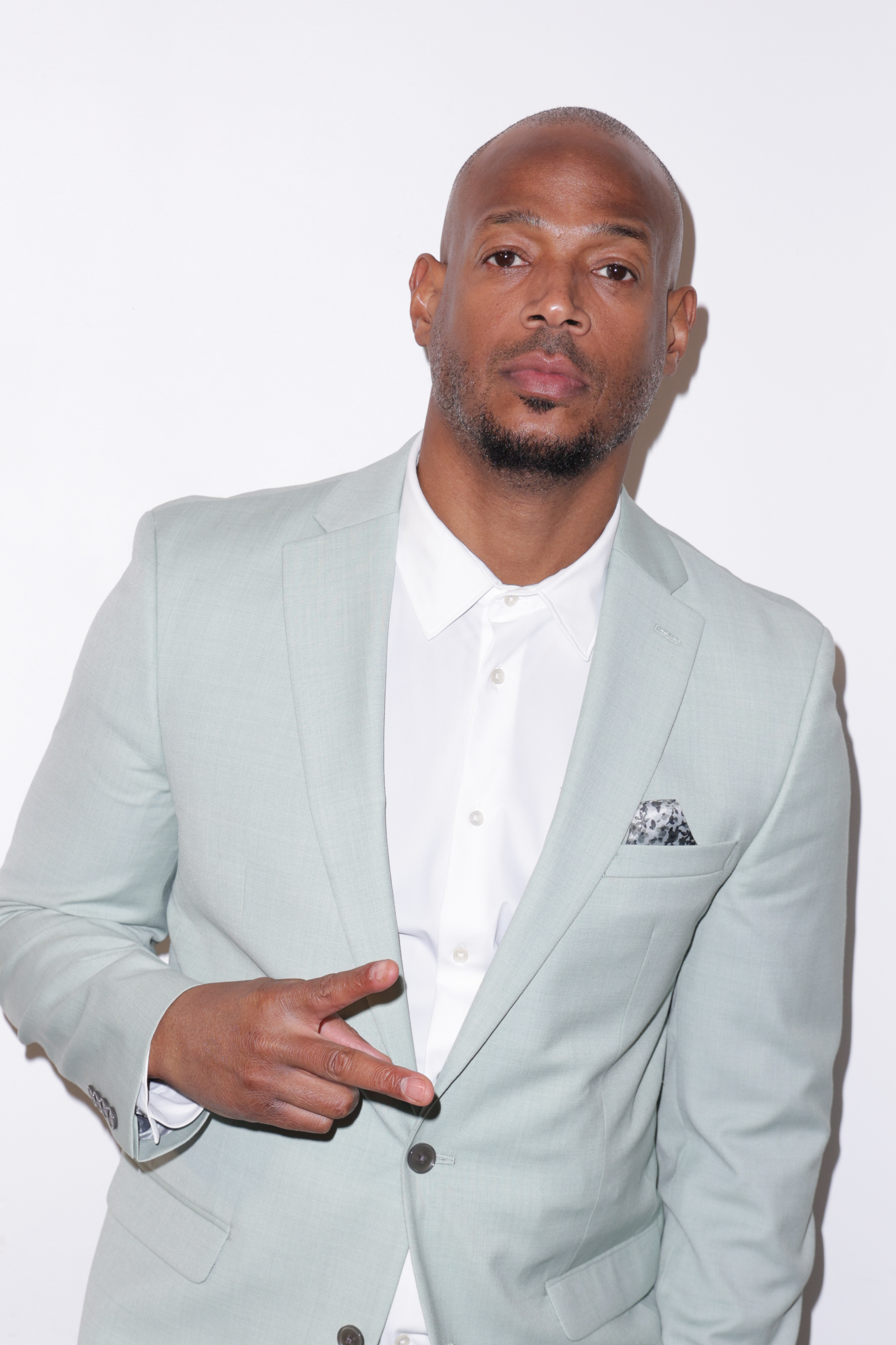 Marlon Wayans posing in a light-colored suit and white shirt, making a peace sign with his right hand