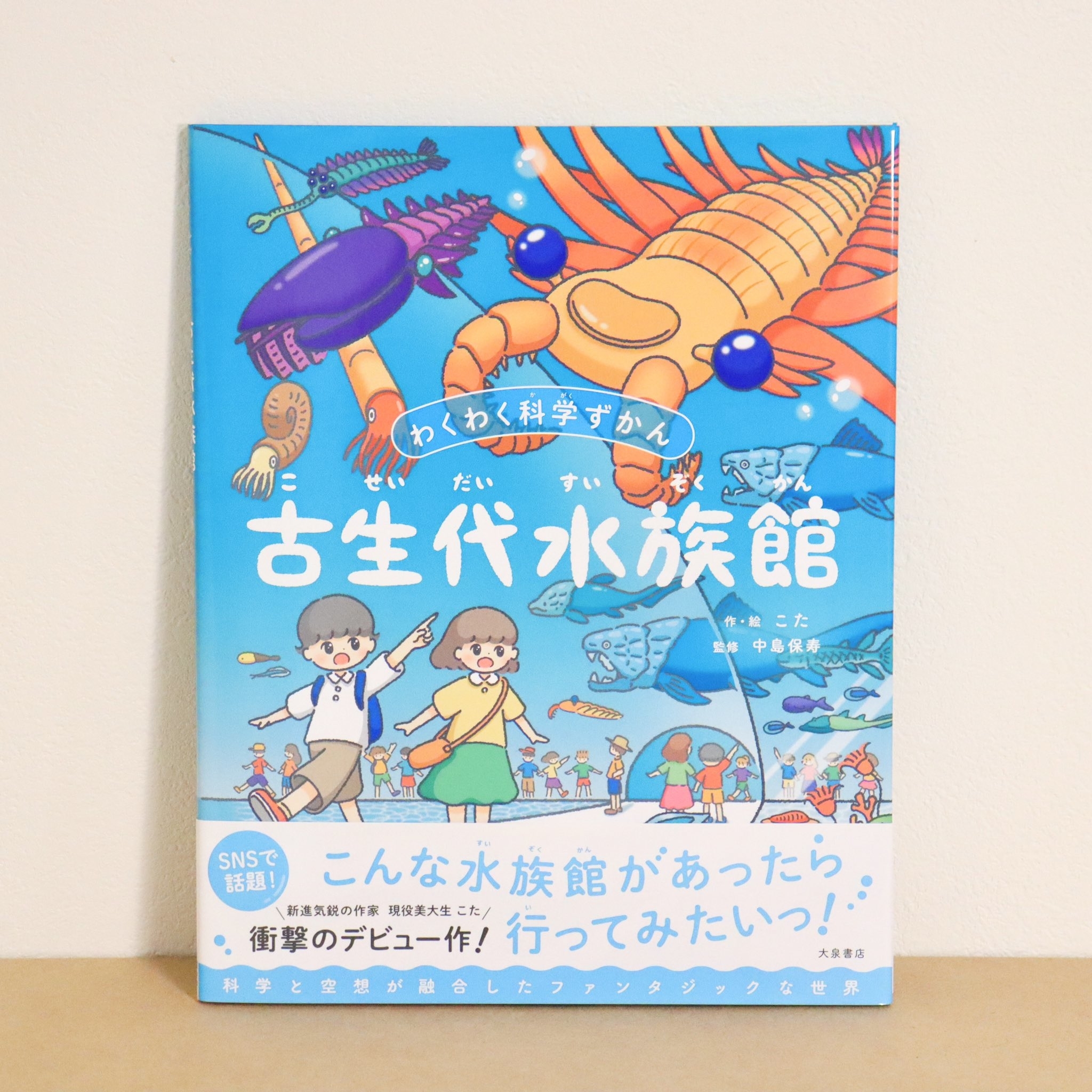 わくわく科学ずかん 古生代水族館の本の表紙が描かれています。表紙には子供たちと古代の海洋生物が描かれています。