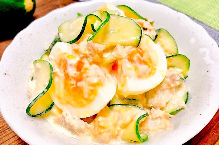 ゆで卵、ツナ、きゅうりのサラダが白いボウルに盛られている。背景にはきゅうりが置かれている。