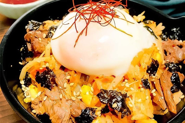 ビビンバのボウル、温泉卵、野菜、肉、のり、ごまが盛られ、美味しそうな韓国料理の一品。