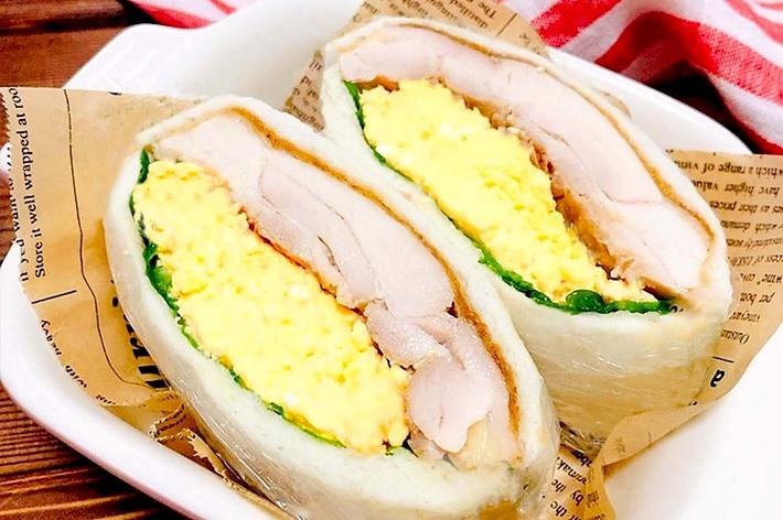 卵サラダとチキンが挟まれたサンドイッチが2つ、お皿の上に盛られています。背景に赤と白のストライプの布が見えます。