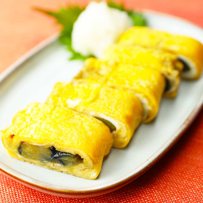 白い皿に盛り付けられた厚焼き卵。背後には大根おろしとシソの葉が添えられている。