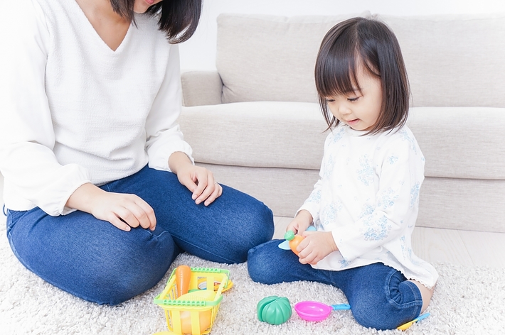 大人と子供がリビングルームのカーペットの上で一緒におもちゃで遊んでいる。