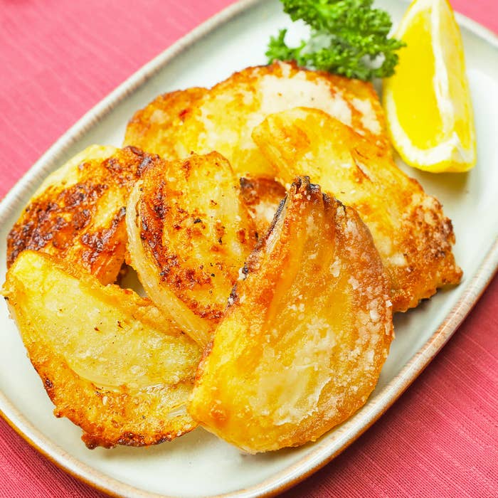 皿に盛られた厚切り玉ねぎ料理、レモンのくさびとパセリの添え物。