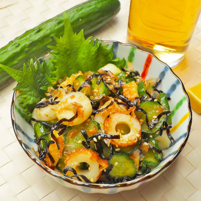 きゅうり、ちくわを使った和風サラダが皿に盛られている。背景にきゅうりと飲み物が写っている。