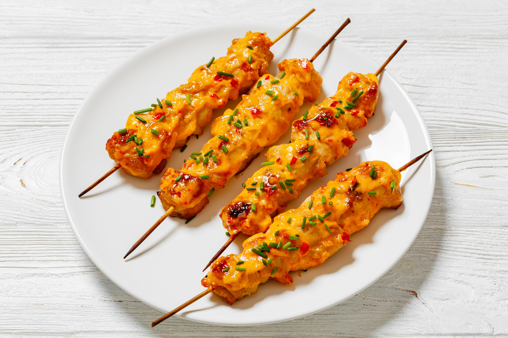 Four grilled chicken skewers topped with herbs and spices on a white plate