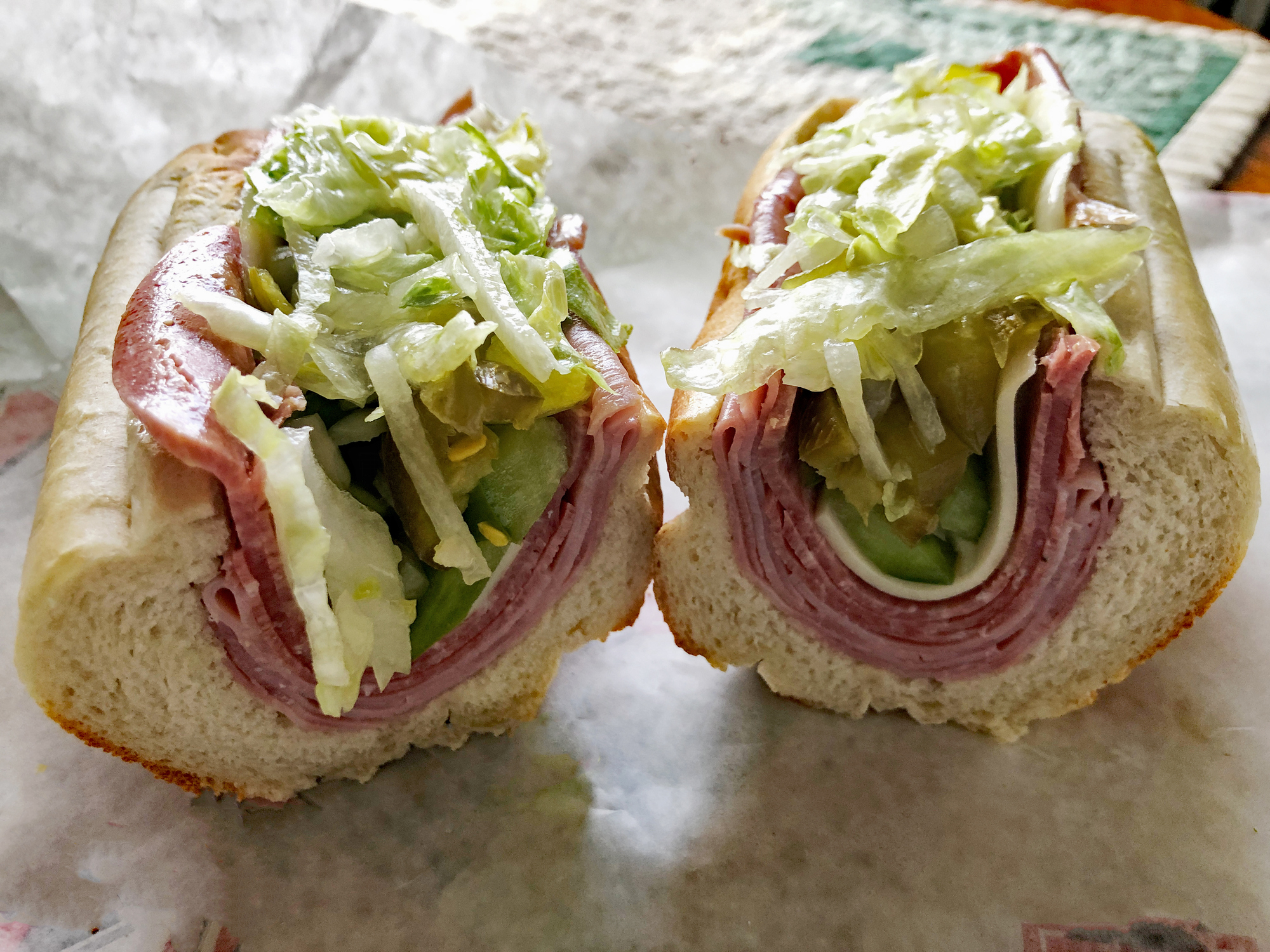 A close-up of a submarine sandwich filled with sliced meats, pickles, cucumber, and shredded lettuce on a sub roll