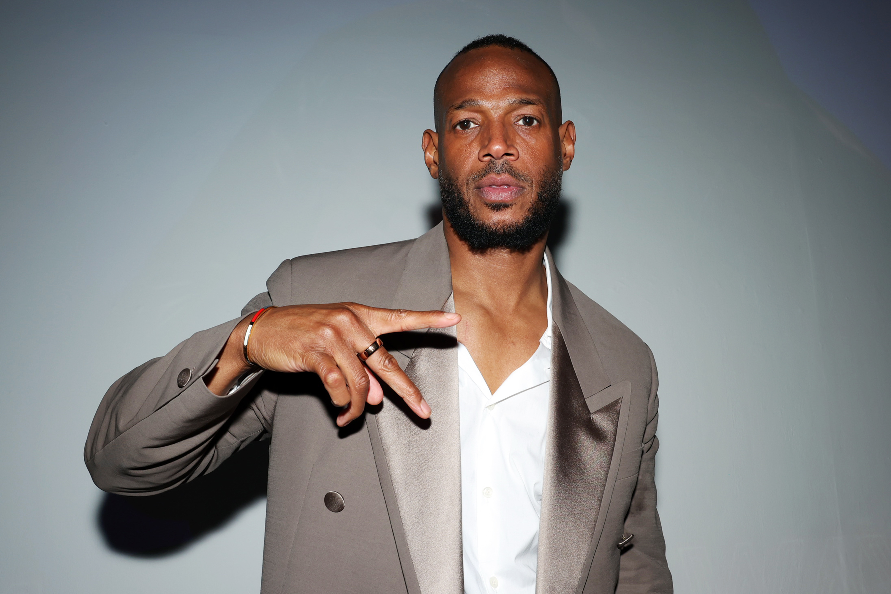 Marlon Wayans dressed in a formal suit, gesturing with his hand, photographed against a plain background