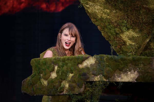 Taylor Swift sings passionately while playing a piano decorated with moss and foliage during a live performance