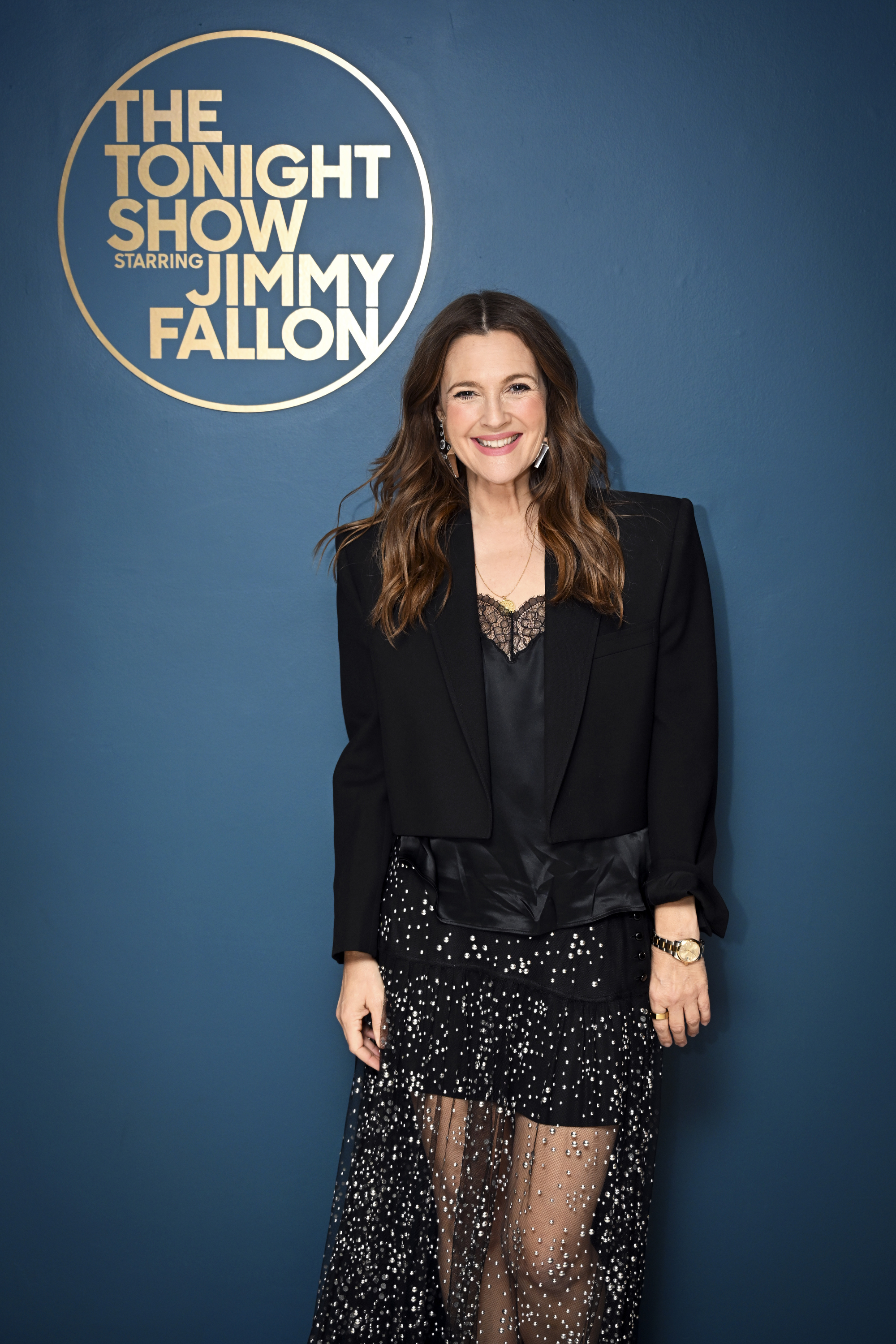 Drew Barrymore on &quot;The Tonight Show Starring Jimmy Fallon,&quot; wearing a black blazer with a sheer, sparkling skirt. She is smiling at the camera