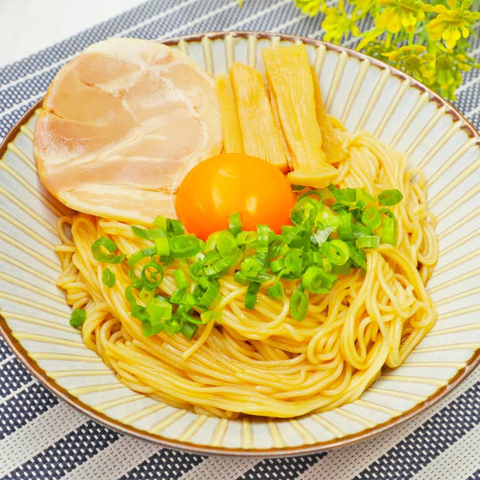 ラーメンの器に麺、チャーシュー、メンマ、生卵の黄身、刻みネギが盛り付けられています。