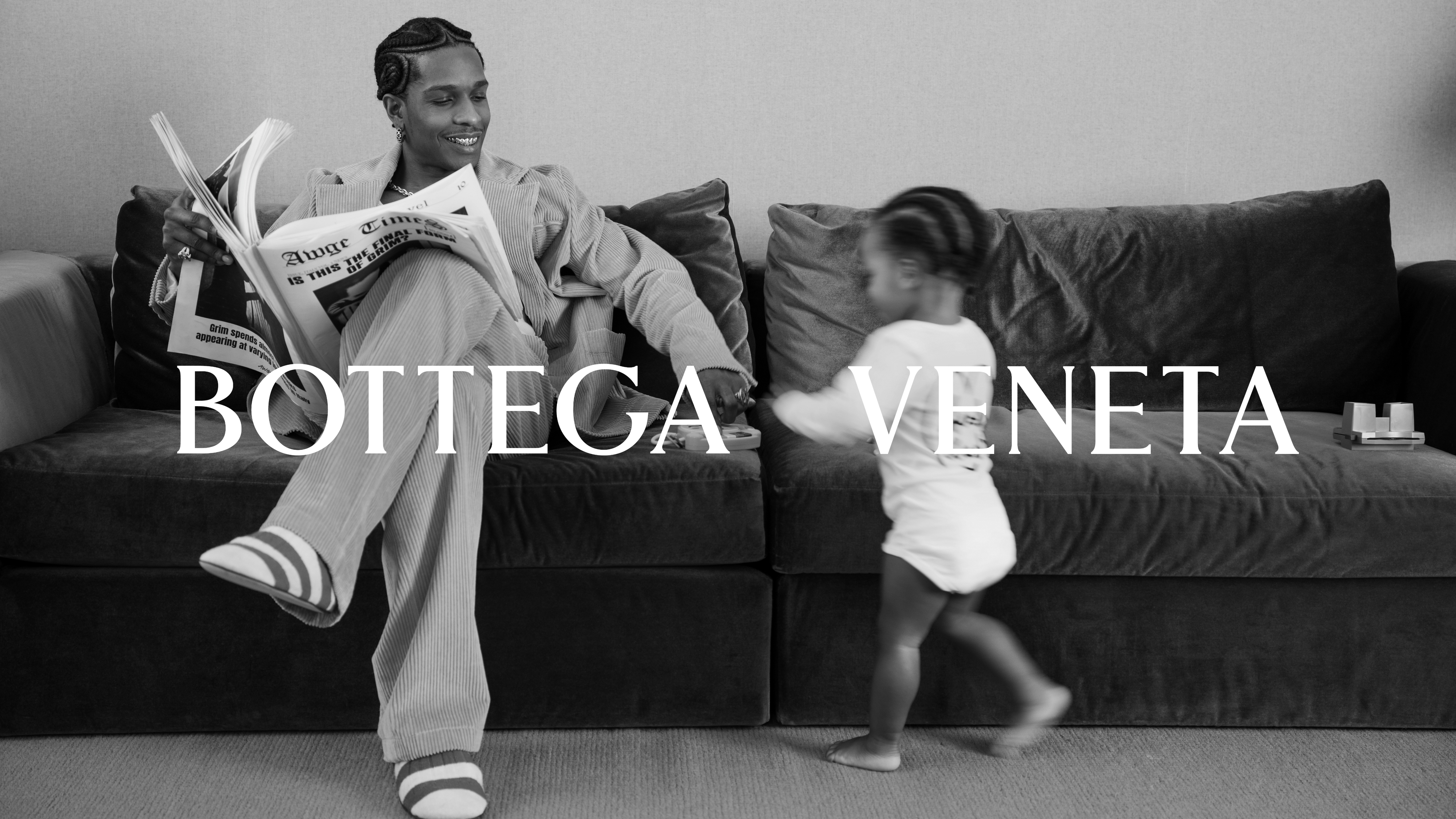 A$AP Rocky reads a newspaper while sitting on a sofa. A child in a T-shirt walks nearby. Text reads, &quot;Bottega Veneta.&quot;