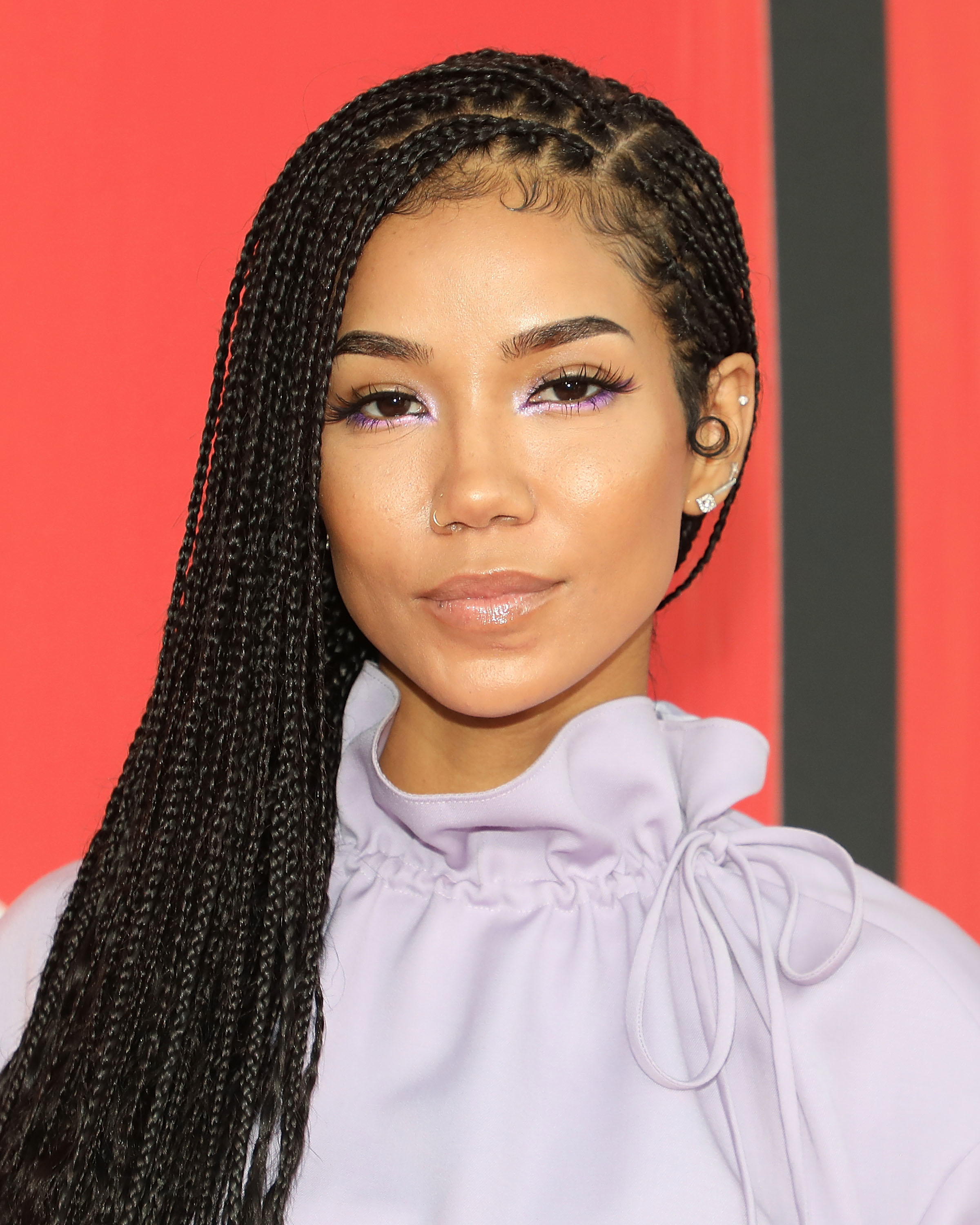 Jhene Aiko on the red carpet, wearing a high-neck, long-sleeve blouse and sporting braided hair