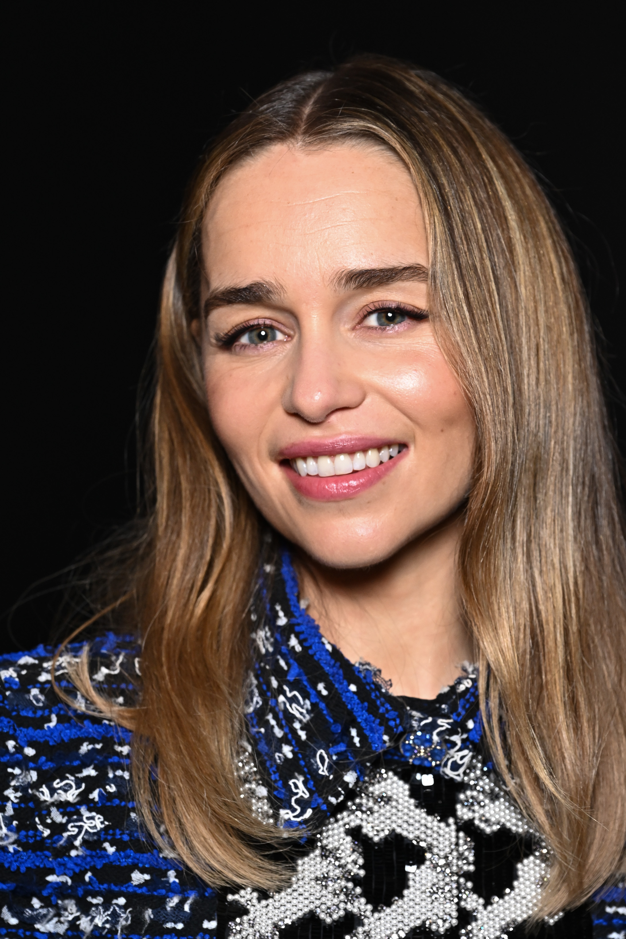 Emilia Clarke smiling, wearing a patterned top with a mix of intricate designs