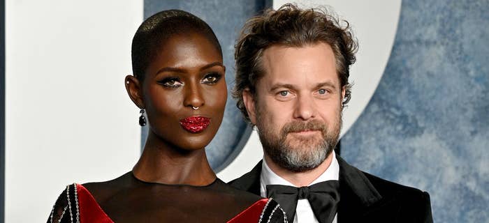Jodie Turner-Smith and Joshua Jackson pose together on the red carpet; Jodie wears an intricate black and red gown with diamond patterns, Joshua wears a classic black tuxedo
