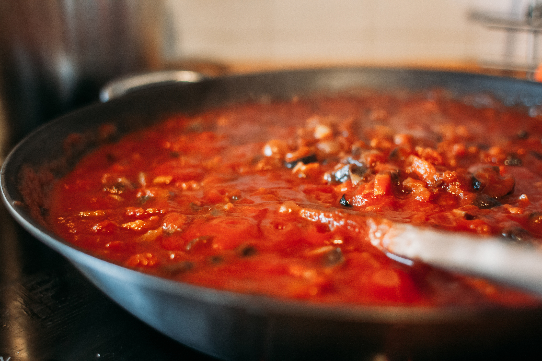 Close-up of a skillet containing simmering tomato sauce with chunks of vegetables and herbs