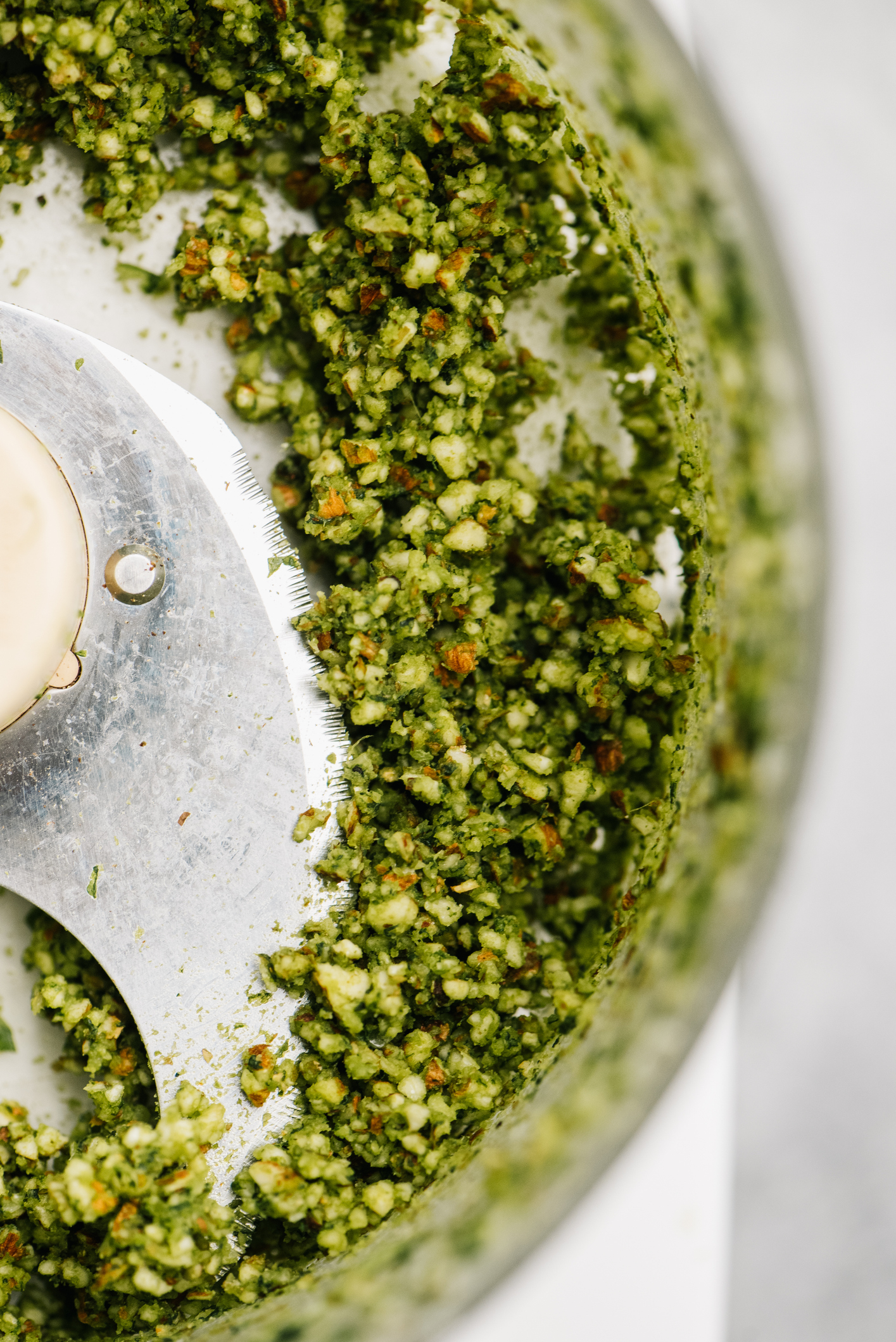 Close-up of a food processor with green pesto-like mixture and a metal blade