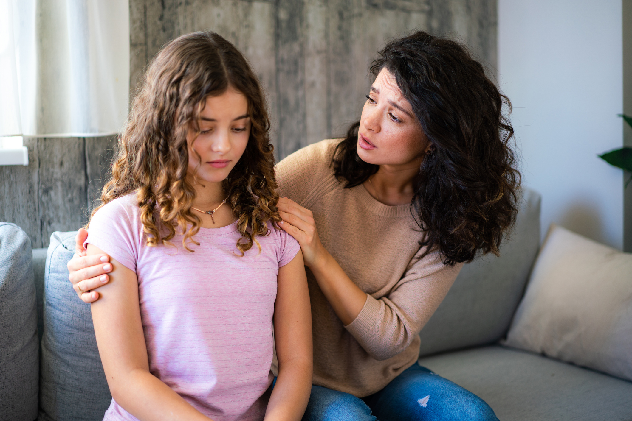 A concerned woman comforts a sad teenage girl, showing support and empathy in a living room
