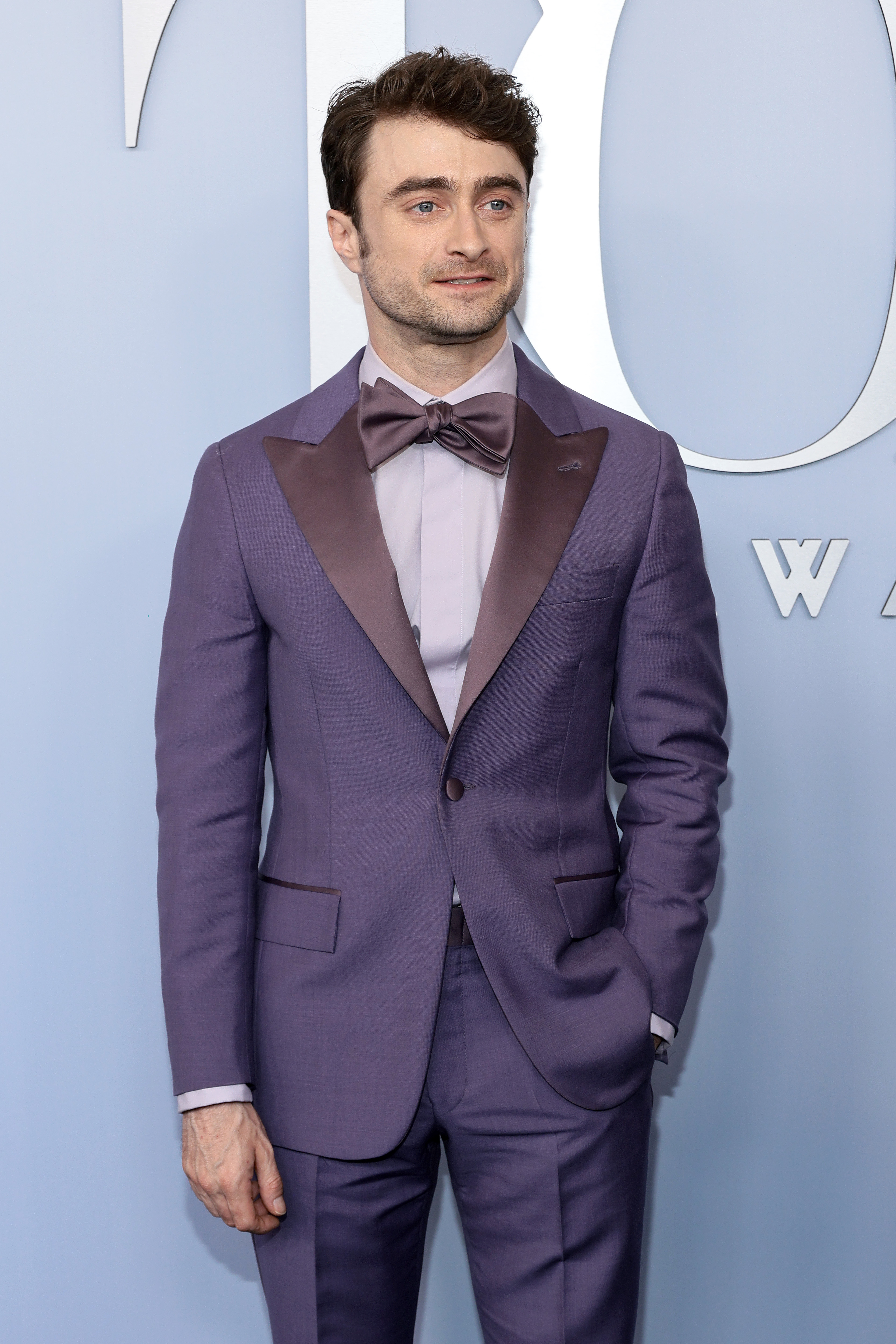 Daniel Radcliffe wearing a tailored suit with a large bow tie, hand in pocket, at a formal event