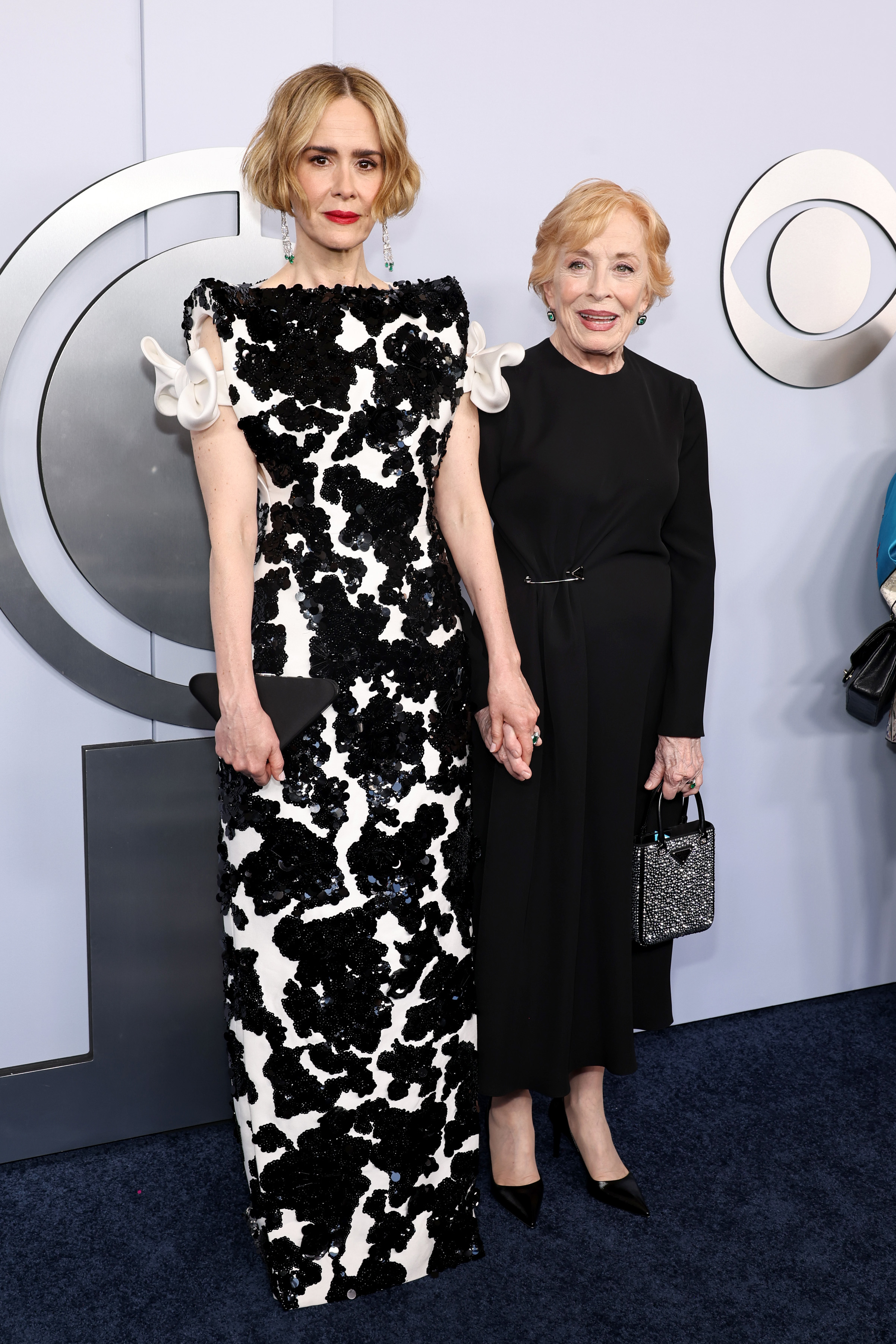 Sarah Paulson in a black and white floral dress and Holland Taylor in a black dress stand together on the red carpet, holding hands