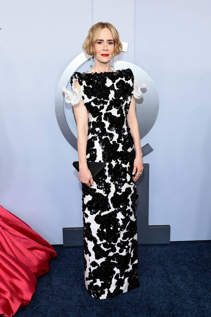 Sarah Paulson in an intricate black and white floor-length gown at a formal event. She has short, styled hair and appears poised with a black clutch
