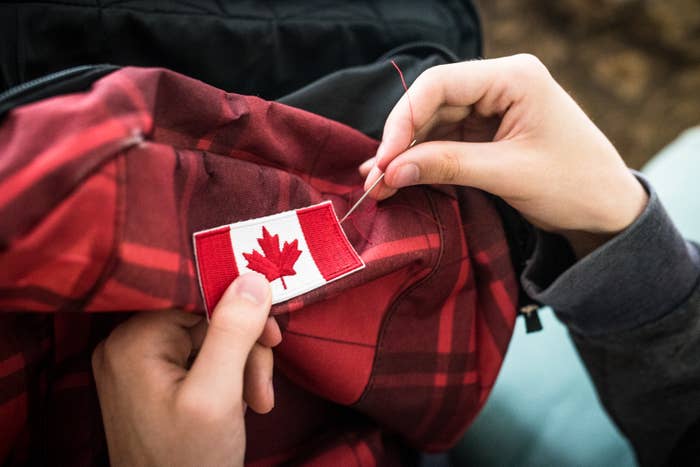 A person is sewing a Canadian flag patch onto a plaid fabric with a needle and thread