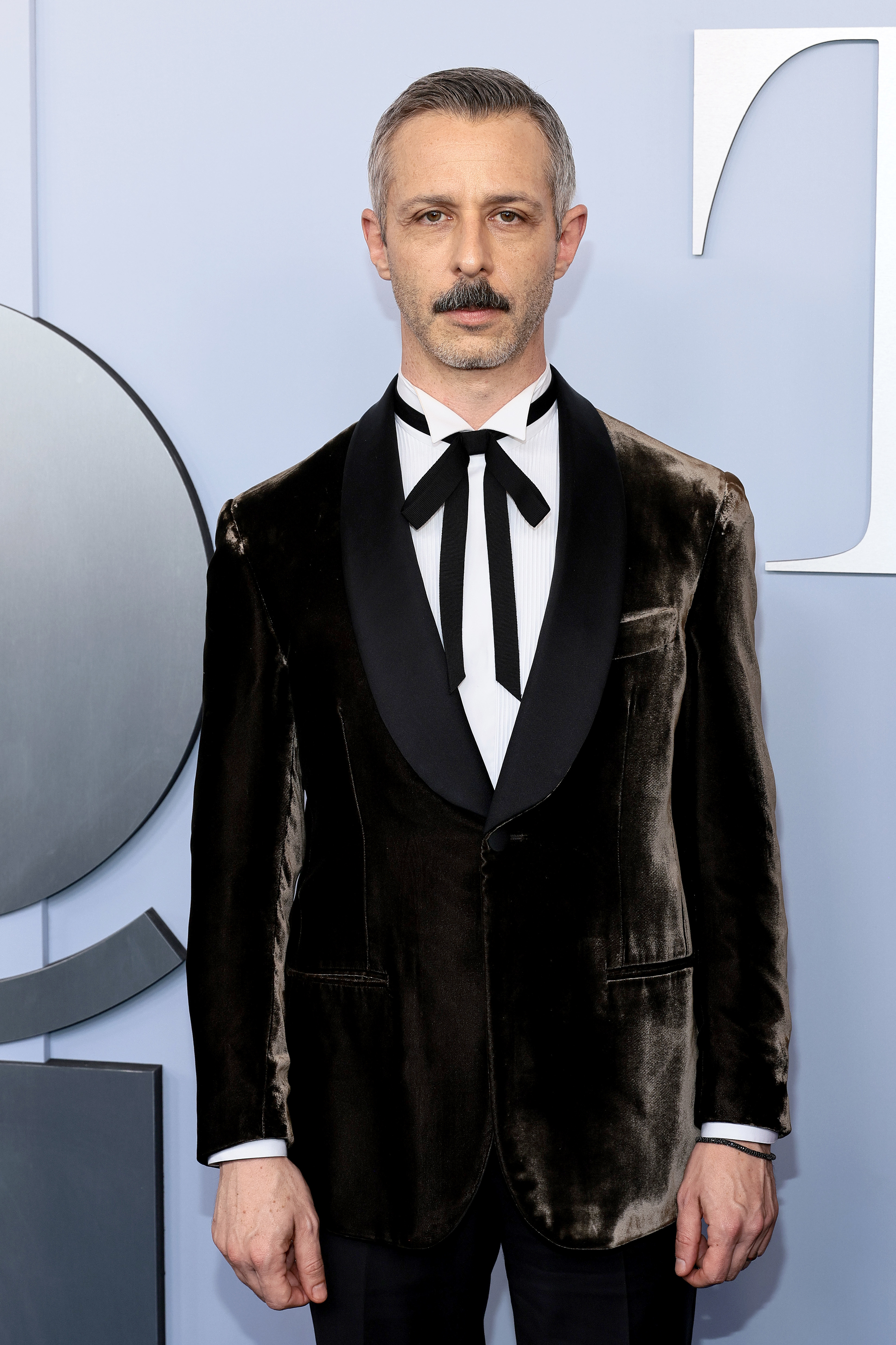 Jeremy Strong on the red carpet, wearing a black velvet tuxedo jacket with a large black bow tie