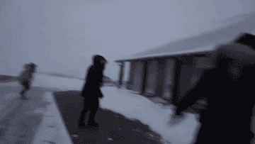People wearing winter coats on a snowy path, one person runs towards the camera, another person walks in the background