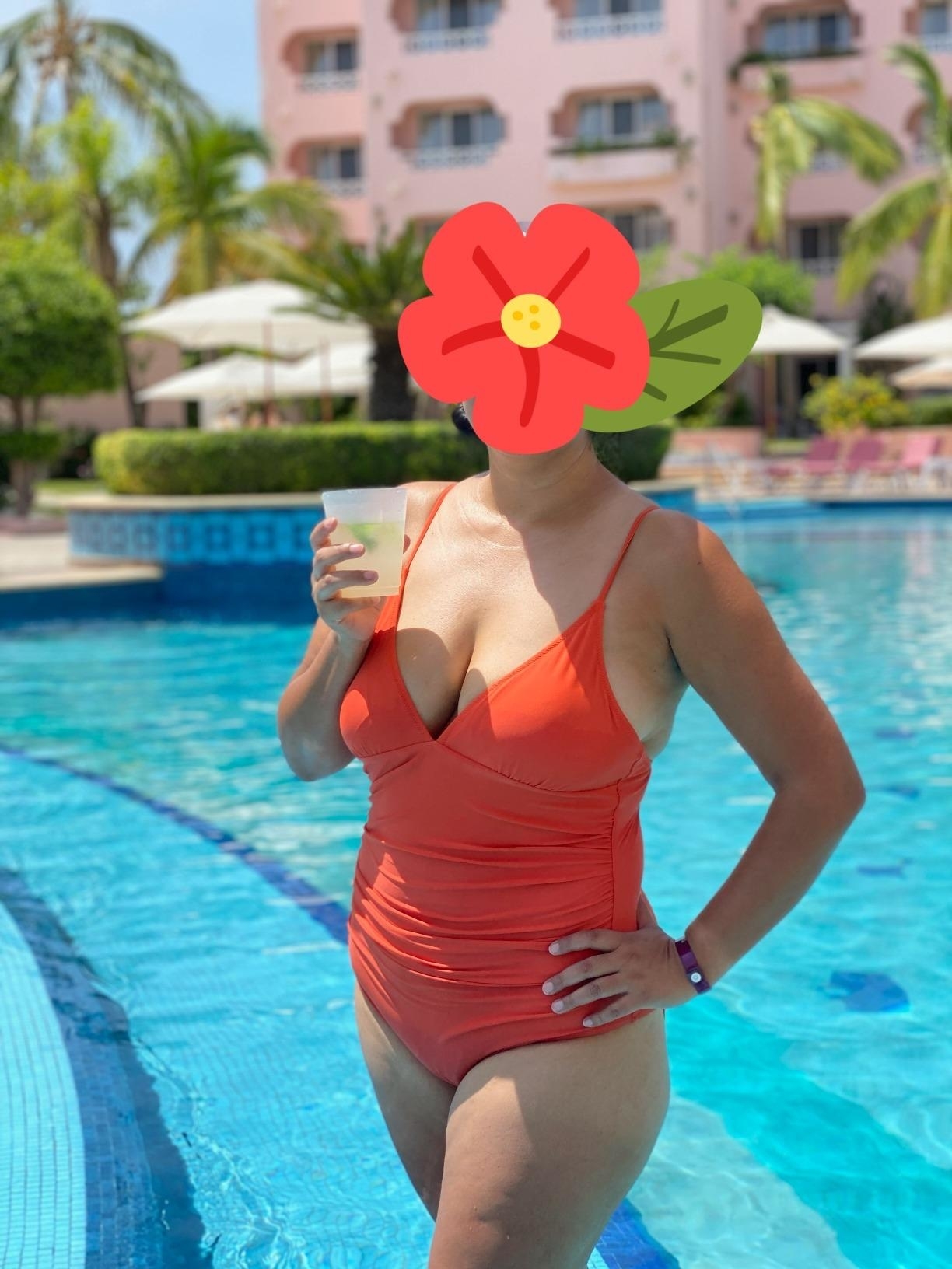 A woman in a swimsuit stands by a pool at a tropical resort, holding a drink