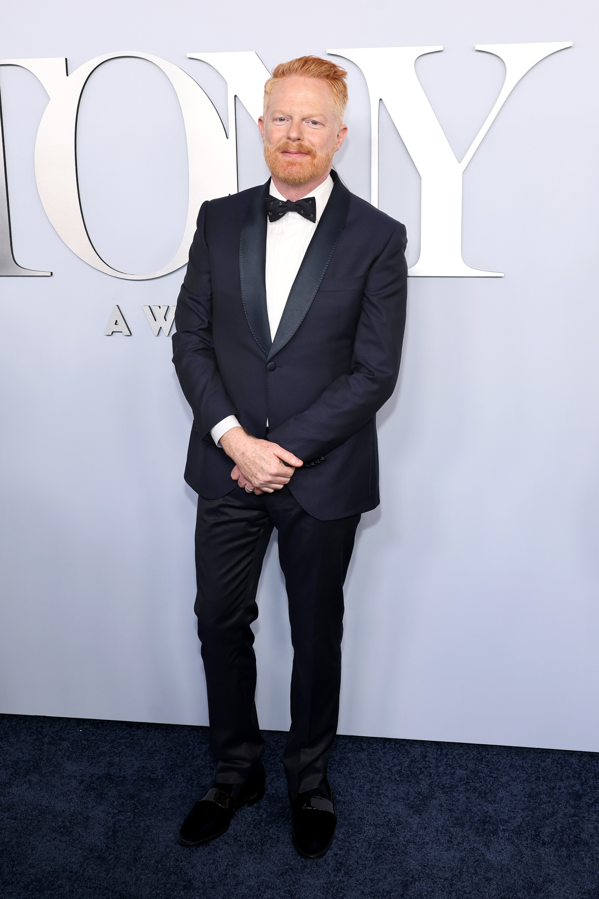 Jesse Tyler Ferguson is standing on a carpet at the Tony Awards, wearing a dark tuxedo with a bow tie