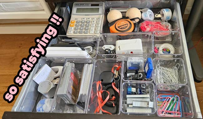 An organized drawer with compartments containing miscellaneous bureau supplies.