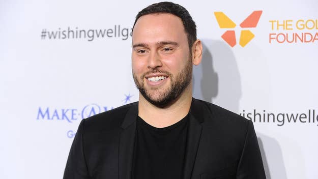 Scooter Braun smiles at a charity event, wearing a black blazer over a black shirt