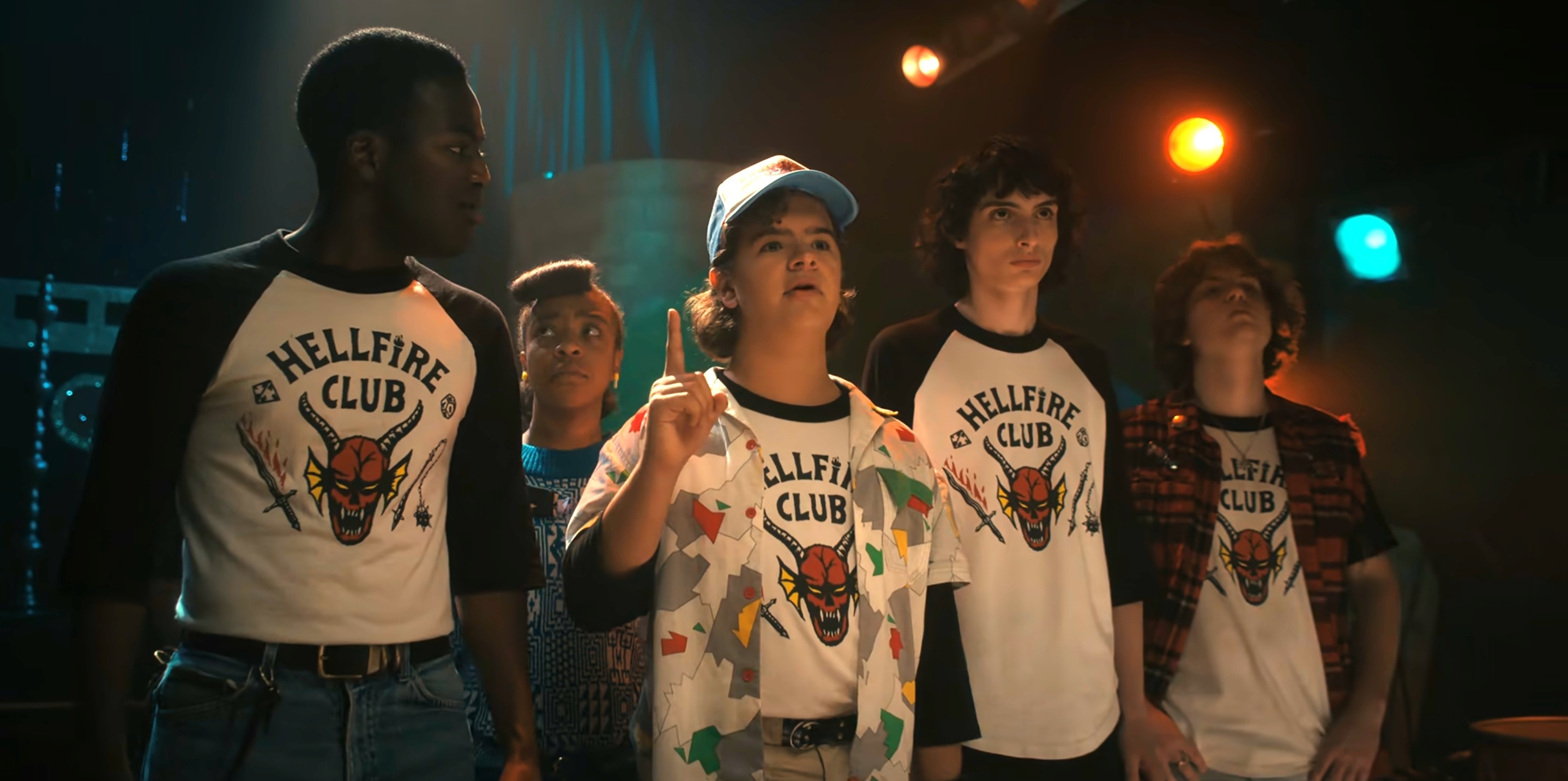 Caleb McLaughlin, Priah Ferguson, Gaten Matarazzo, Finn Wolfhard, and Millie Bobby Brown wear 'Hellfire Club' shirts in a scene from Stranger Things